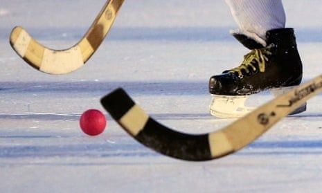 Närbild av bandyklubbor, skridsko och röd boll på isen